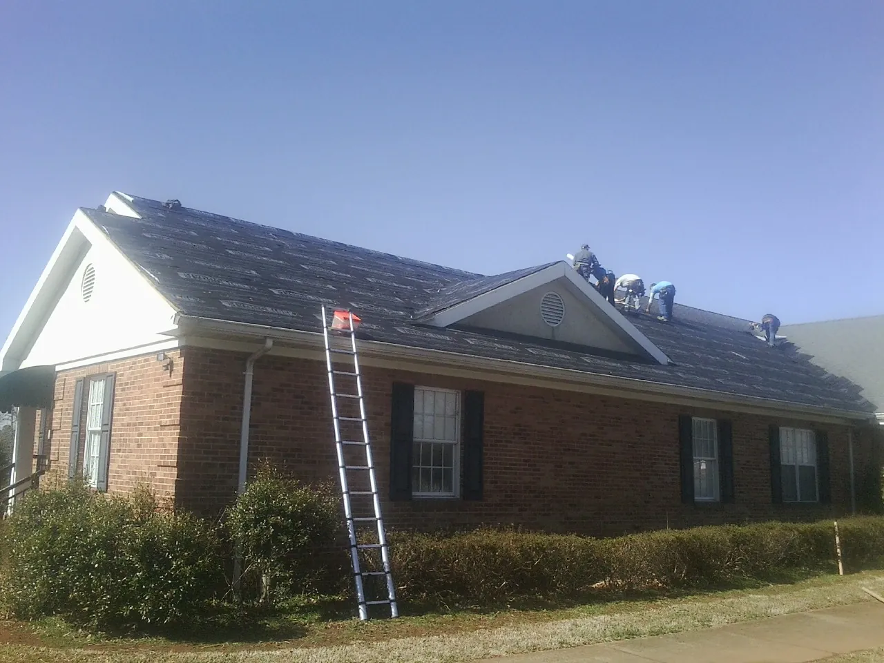 Crew tearing shingles off a brick ranch roof with a ladder set — Metal Roof Repair work by our crew in Hopewell